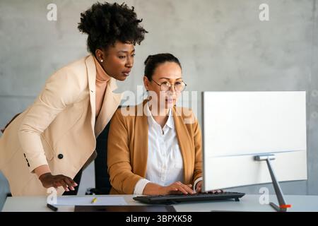 Team creativo composto da donne di successo multietnico che guardano il computer alla propria scrivania in un ufficio moderno Foto Stock