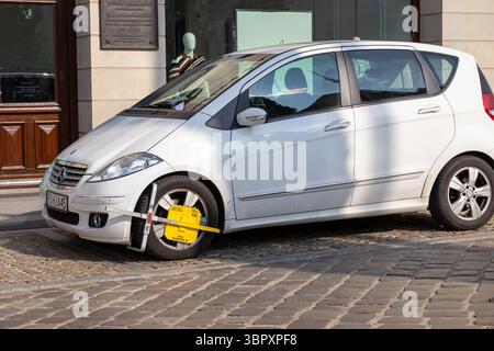 Poznan, Polonia - 18 giugno 2025: Auto bianca con un prominente morsetto per ruota giallo, che mostra le conseguenze delle violazioni dei parcheggi in città Foto Stock