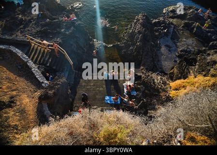 Persone che nuotano nelle piscine naturali costiere con le montagne di Los Gigantes e le scogliere in lontananza, Puerto de Santiago, Tenerife, Isole Canarie, Spagna Foto Stock