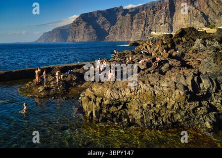 Persone che nuotano nelle piscine naturali costiere con le montagne di Los Gigantes e le scogliere in lontananza, Charco de Isla Cangrejo, Tenerife, Isole Canarie, Spagna Foto Stock