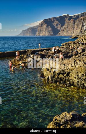 Persone che nuotano nelle piscine naturali costiere con le montagne di Los Gigantes e le scogliere in lontananza, Charco de Isla Cangrejo, Tenerife, Isole Canarie, Spagna Foto Stock