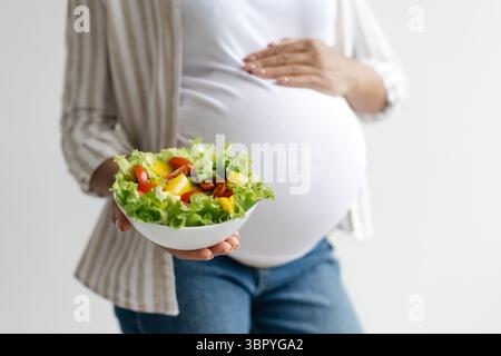 Primo piano di una donna incinta nera che tiene una ciotola di insalata fresca Foto Stock