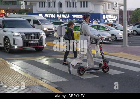 Uomo che attraversa un passaggio pedonale su uno scooter elettrico, Abu Dhabi, Emirati Arabi Uniti Foto Stock