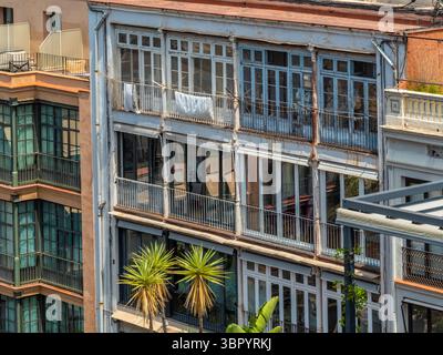 Un vecchio edificio residenziale con balconi in vetro chiusi, conosciuti come "galerias", una caratteristica architettonica tipica di Barcellona, Spagna. Foto Stock