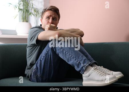Uomo che soffre di paranoia sul divano a casa Foto Stock