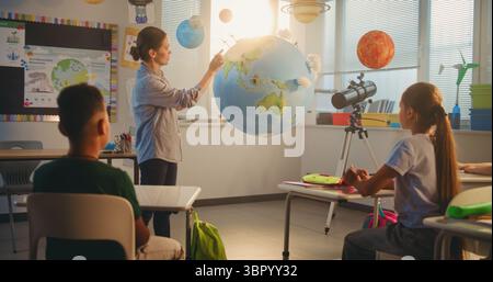 Lezione di scienza: Insegnante femminile che educa i bambini intelligenti usando il modello del pianeta Terra. Scuola primaria i bambini che studiano energia rinnovabile e sistema solare in una moderna aula multietnica. Educazione STEM. Foto Stock