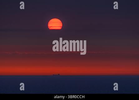 Incredibile tramonto sul mare vicino alla Danimarca, catturato da una nave da crociera. Le turbine eoliche sagomano l'orizzonte sotto i cieli rossi e arancioni. Foto Stock