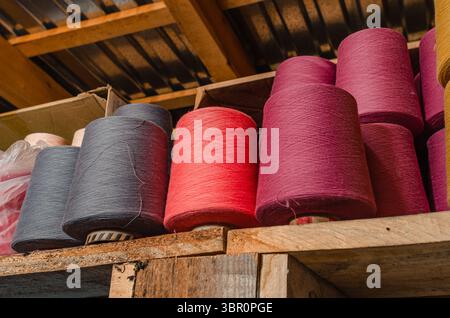 Filetti a maglia multicolore su ripiano in legno. Bobine colorate di filo nella fabbrica di calze. Produzione di calzini Foto Stock