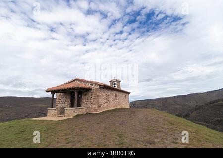 Piccola chiesa in pietra con tetto in piastrelle e campanile in piedi sulla collina che si affaccia sulla valle nella campagna spagnola Foto Stock