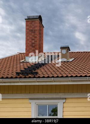 Vista ravvicinata del tetto di una casa svedese con camino in mattoni, scale di sicurezza e finestra. Foto Stock