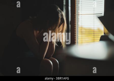 Donna turbata che copre il viso mentre si siede sul bagno. Foto Stock