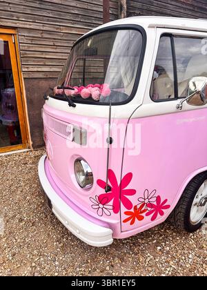 Camper vintage Volkswagen Transporter T3 rosa con decorazioni floreali utilizzate per le fotografie di matrimoni su vialetto di ghiaia e rustico edificio in legno Foto Stock