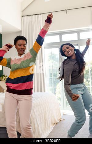 Diverse amiche che ballano accanto al letto con una coperta testurizzata sul pavimento tappezzato dalla finestra. Giocoso, amicizia, stile di vita, rilassante, vivace, cheerf Foto Stock
