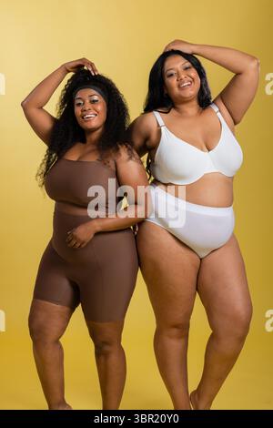 Diverse amiche che posano in studio indossando reggiseno sportivo marrone, pantaloncini da bici, reggiseno bianco e slip. Atletica, fiducia, empowerment, diversità, wel Foto Stock