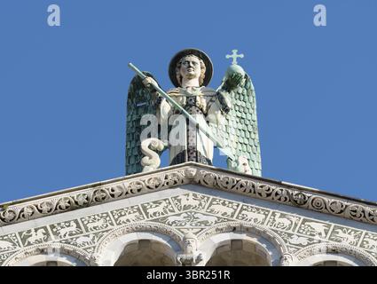 Statua dell'Arcangelo Michele con ali, spada e croce in cima alla Chiesa di San Michele in foro, Lucca, Italia, fiancheggiata da due angeli di bronzo. Foto Stock