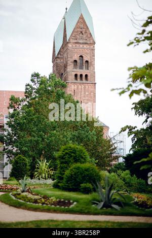 Un bellissimo giardino con varie piante e fiori in primo piano, caratterizzato da un'alta e storica torre in pietra sullo sfondo. La torre ha un verde Foto Stock