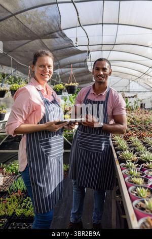 Diversi colleghi che tengono le compresse che tendono a filari succulenti in serra con tubi di irrigazione a goccia. Giardinaggio, collaborazione, moderno, ambiente, crescere Foto Stock