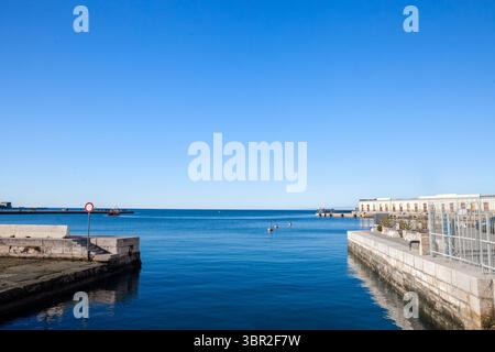 Il luminoso panorama mattutino del Mare Adriatico dalle banchine del porto di Trieste, in Italia, mostra acque blu tranquille, boe di ormeggio nel canale, pilota distante Foto Stock