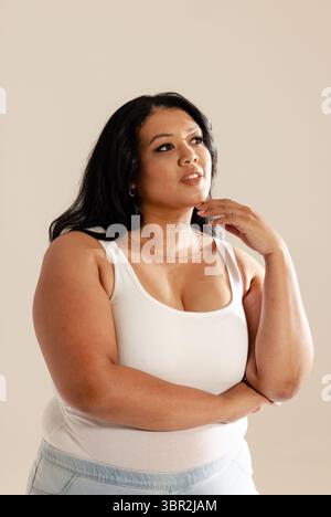 Donna asiatica in piedi sullo sfondo beige con canotta bianca, jeans leggeri e gioielli Foto Stock