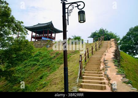 Gongju, Corea del Sud - 13 giugno 2025: Una ripida serie di gradini di legno sale su un pendio erboso accanto ad un padiglione in cima alla storica Fortezza di Gongsanseong su una Foto Stock