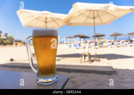 Un bicchiere di birra fredda siede su un tavolo in un resort sulla spiaggia, offrendo una fuga rinfrescante sotto il sole estivo Foto Stock