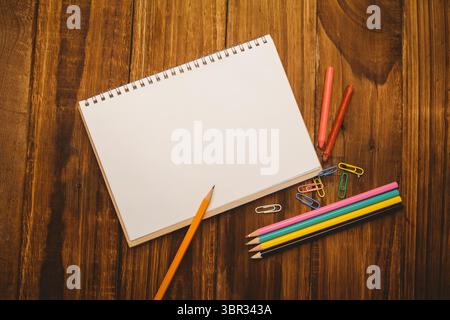 Sketchbook è appoggiato su una scrivania in legno in stile vettoriale piatto con matite colorate, pastelli e graffette Foto Stock