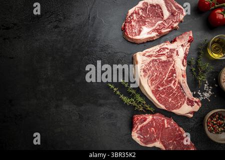 Varietà di bistecche fresche di carne cruda Black Angus prime T-Bone, New York, Ribeye e stagionatura su sfondo nero, vista dall'alto Foto Stock