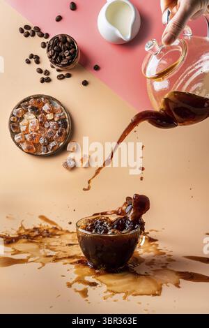 Versare il caffè in una tazza creando schizzi di ingredienti su sfondo arancione e rosa Foto Stock