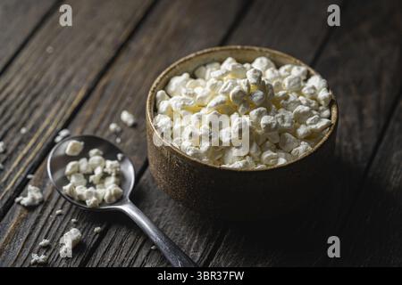 Contadini ricotta formaggio in una ciotola di argilla, accanto ad un cucchiaio su sfondo di legno scuro, Close-up. Naturale cibo sano, sano cibo sano sano sano Foto Stock
