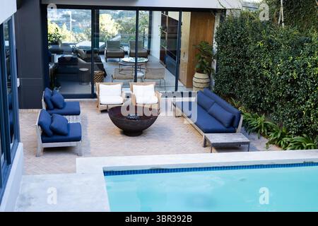 Patio sul retro con caminetto circolare e sedie bianche e piscina davanti Foto Stock