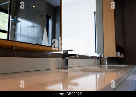 Rubinetti cromati che risplendono su un piano lavabo in quarzo bianco nel bagno con porta doccia in vetro Foto Stock