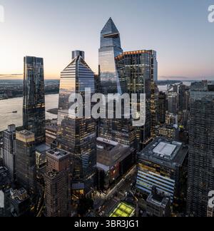 Vista aerea dei grattacieli torreggianti che piergono il cielo crepuscolo, le loro facciate di vetro riflettono la luce che svanisce sul fiume Hudson, New York, Stati Uniti. Foto Stock