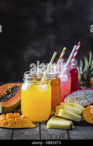 Bicchieri di gustosi succhi tropicali freschi con frutta tropicale fresca, Papaya Pine Apple Mango Dragon su sfondo scuro Foto Stock