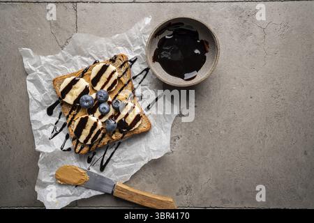 Toast al burro di arachidi con fette di banana e cioccolato. Colazione sana o snack su sfondo grigio di cemento. Vista dall'alto Foto Stock