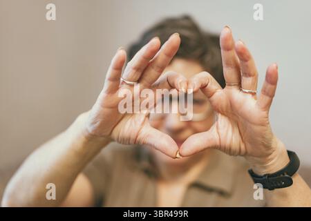 Carino anziana donna che fa una forma del cuore con lei mani e dita Foto Stock