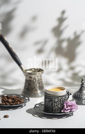 Caffè in metallo turco tradizionale tazza e caffè in chicchi su sfondo bianco con ombre Foto Stock
