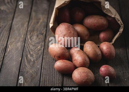 Patate rosse crude nuove in sacchi di carta su sfondo di legno Foto Stock