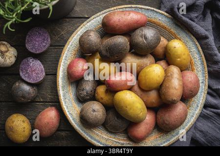 Varie varietà di nuove patate colorate, bianche, rosse e viola su sfondo di legno scuro, vista dall'alto Foto Stock