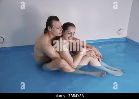 Ragazzo e fidanzata uno accanto all'altro in piscina, in acqua con sale marino. Concetto flottante Foto Stock