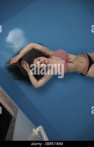 Draufsicht auf eine attrattivo junge Frau, die auf blauem Wasser schwimmt. Entspannung und Wellness-Therapie. Raum kopieren Foto Stock