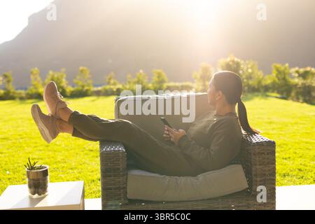 Poltrona in vimini che riposa sul patio illuminato dal sole e si affaccia sul prato e sulle colline, con succulento riposo sul tavolo Foto Stock