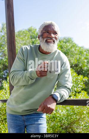 Senior uomo afroamericano in felpa verde e jeans in piedi sul ponte che reggono tazza in ceramica grigia Foto Stock