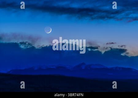 6 aprile 2019: La luna crescente di 2 giorni sopra la catena delle Montagne Rocciose nel sud dell'Alberta, vista dall'Osservatorio astrofisico di Rothney, il 6 aprile 2019. Earthshine è visibile sul lato notturno della Luna... si tratta di una miscela HDR di 5 esposizioni tra parentesi con l'obiettivo da 200 mm a f/2,8 e Sony a7III a ISO800. Miscelato con ACR. La gamma di esposizione cattura il primo piano scuro senza soffiare fuori il cielo e la Luna luminosi. Ho applicato maschere di luminosità per regolazioni locali al cielo e al suolo. Ho aggiunto un leggero effetto bagliore Orton al terreno e nuvole per un effetto artistico Foto Stock