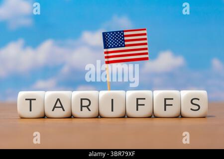 I cubi che scrivono "TARIFFE" sono disposti in linea con una piccola bandiera americana. Concetto di tariffe, in particolare in relazione agli Stati Uniti. Foto Stock
