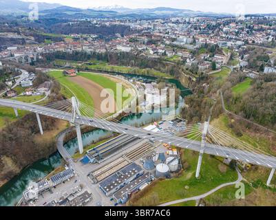 Vista aerea dell'elegante e moderno ponte Pont de la Poya che attraversa il paesaggio, contrastando con il tortuoso fiume e il paesaggio urbano lontano, Friburgo, Svizzera. Foto Stock