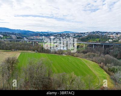 Veduta aerea del Pont de la Poya che si innalza su vivaci campi verdi, giustapposta al lontano skyline di Friburgo, Friburgo, Svizzera. Foto Stock