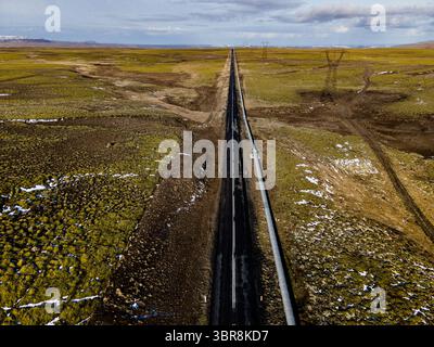 Vista aerea di una strada dritta e aspra che attraversa un paesaggio roccioso, un nastro di asfalto sotto un vasto cielo, Mosfellsbær, Islanda. Foto Stock
