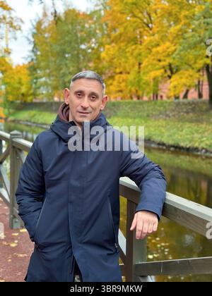 L'uomo con un cappotto nero sta su un ponte. Sta sorridendo. Il ponte è vicino a un fiume Foto Stock