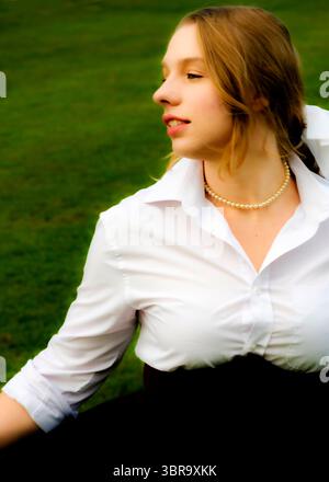 Una donna con camicia bianca e collana di perle guarda lateralmente. Foto Stock