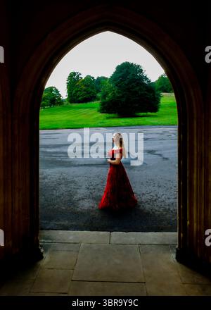 Una donna con un vestito rosso si trova di fronte a un campo verde, incorniciato da un arco. Foto Stock